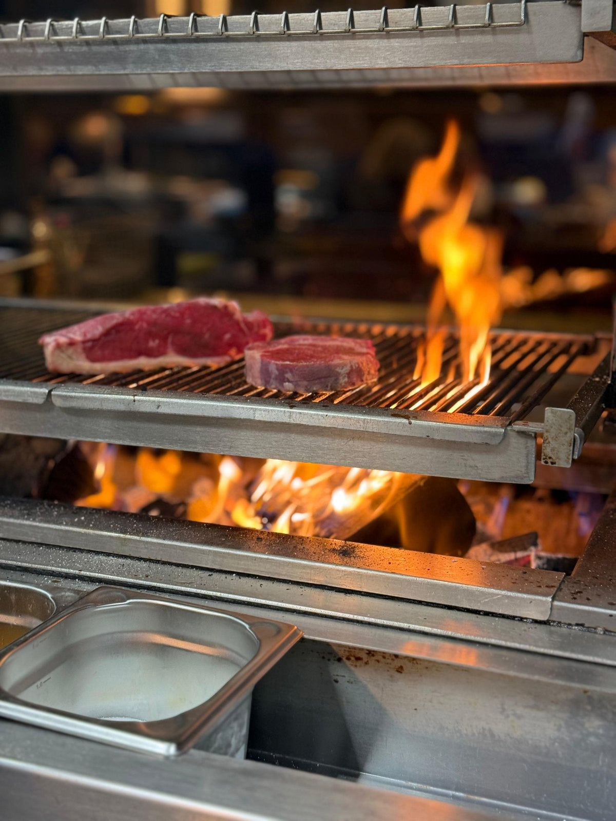 Steaks searing over a live charcoal fire in a professional grill