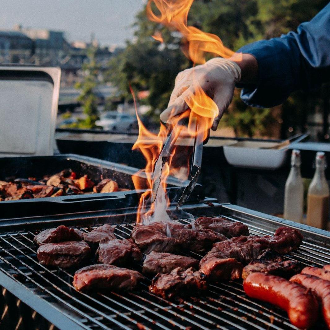 Person grilling meat on a barbecue with flames